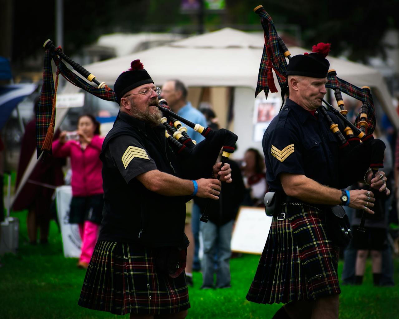 Scottish bagpipers in kilts performing at an outdoor festival.