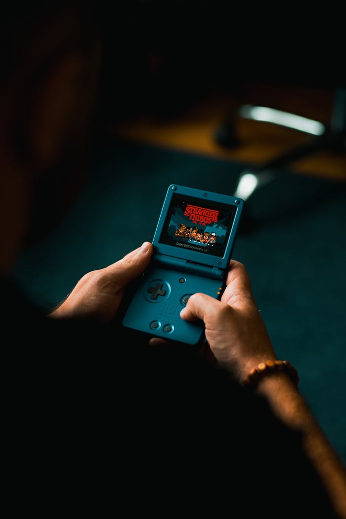 services-02 Close-up of individual holding a retro handheld gaming device, playing a classic video game indoors.