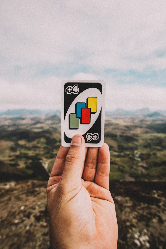 A person holds a colorful card against a picturesque mountain landscape, blending game and nature.