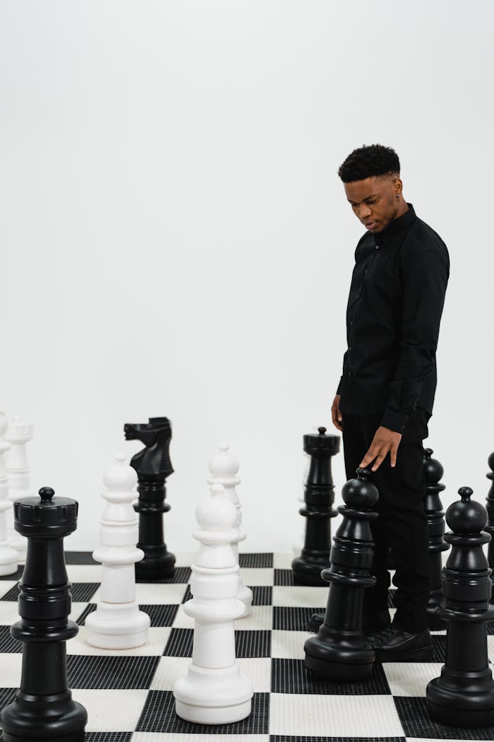 services-01 A young man in black contemplates his move on a large chessboard with oversized pieces.